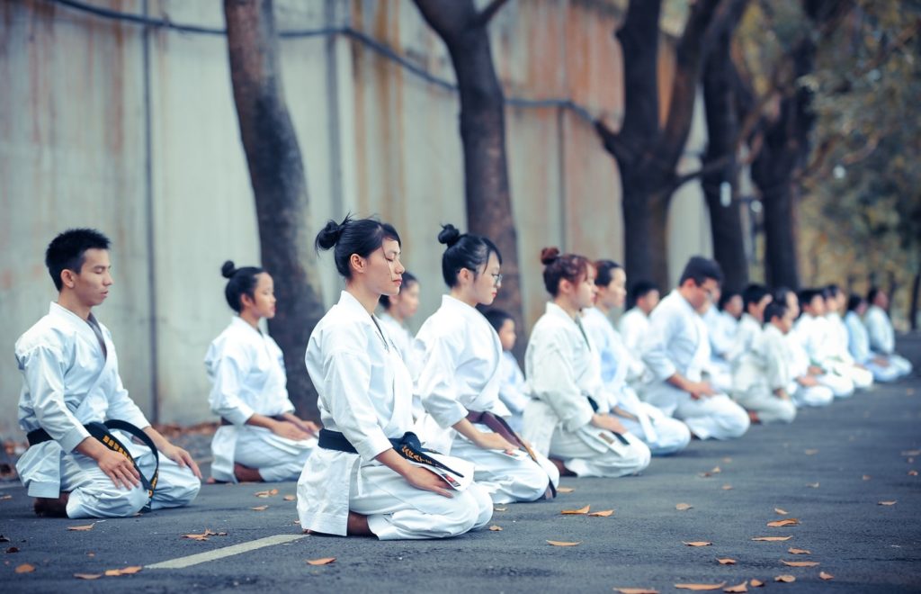 Karate class kneeling down with eyes closed in a park